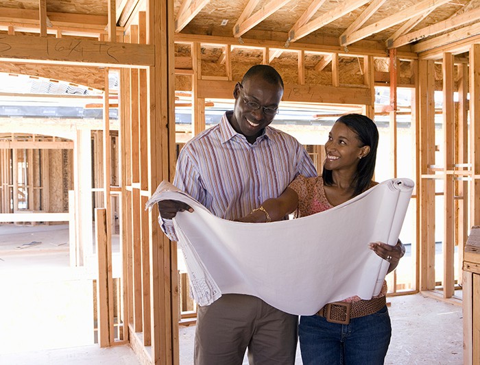 Couple reading house blueprints while standing inside home that is under construction