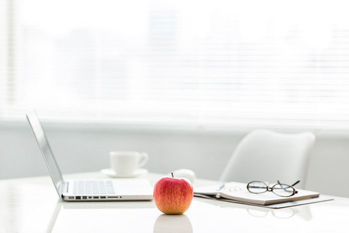 Laptop, notebook, cup and saucer, eyeglasses and apple sitting on table