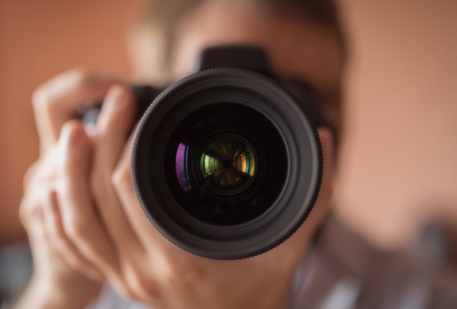 Camera lens in focus with person holding camera blurred in the background