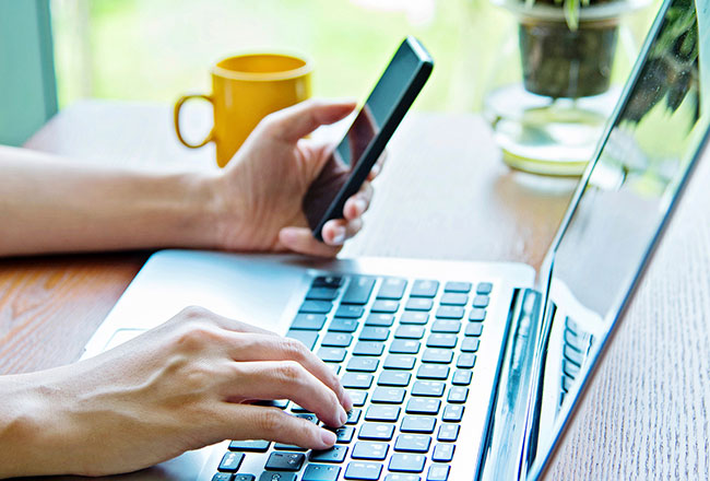 Hands holding cell phone and typing on computer keyboard