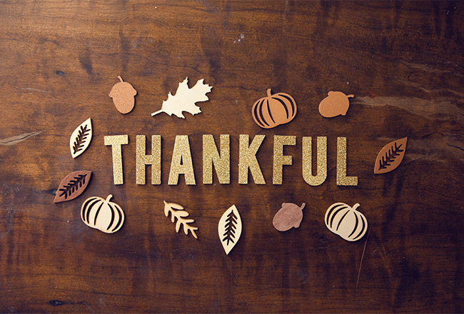 Words "thankful" and cut outs of fall leaves, acorns and pumpkins on wooden table