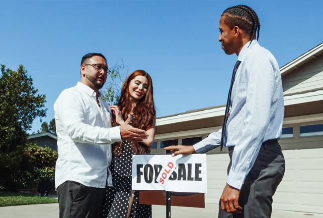 Couple and agent standing around 'For Sale' sign on front lawn