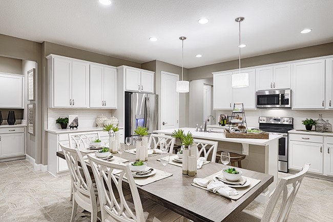 White kitchen with dining table in the foreground, kitchen island and cabinets in the background