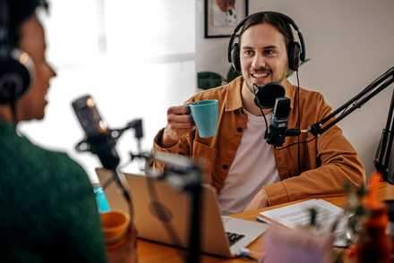 Man and woman wearing headphones and speaking into microphones, recording a real estate podcast.