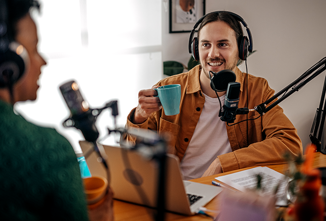Man and woman wearing headphones and speaking into microphones, recording a real estate podcast.