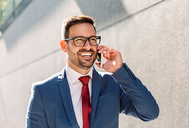 Person with glasses in suit outside laughing while on cell phone