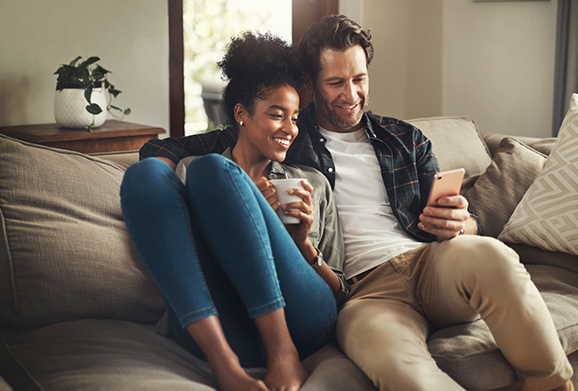 First-time homebuyers sitting on sofa and looking at cell phone