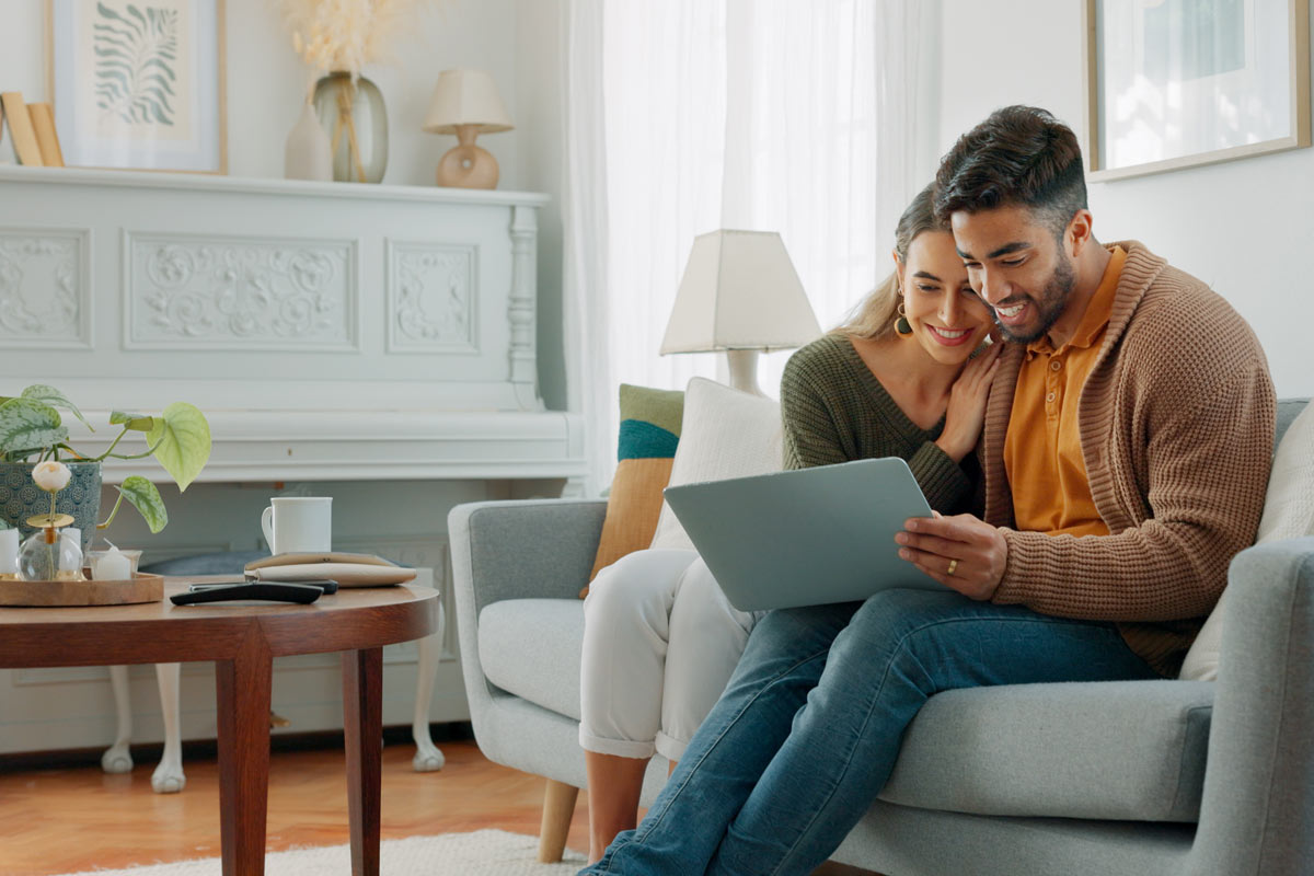 Man typing on laptop with women smiling, looking over his shoulder