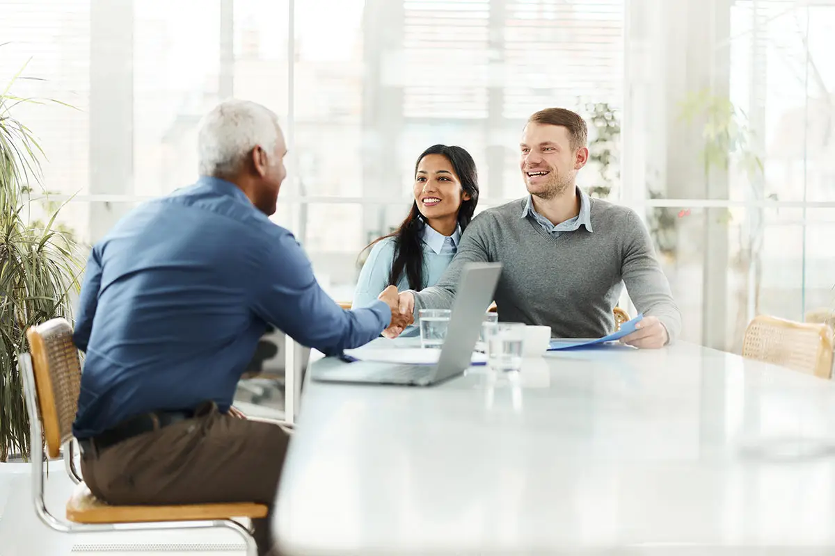 Real estate agent with shaking hands with a homebuyer couple at a desk