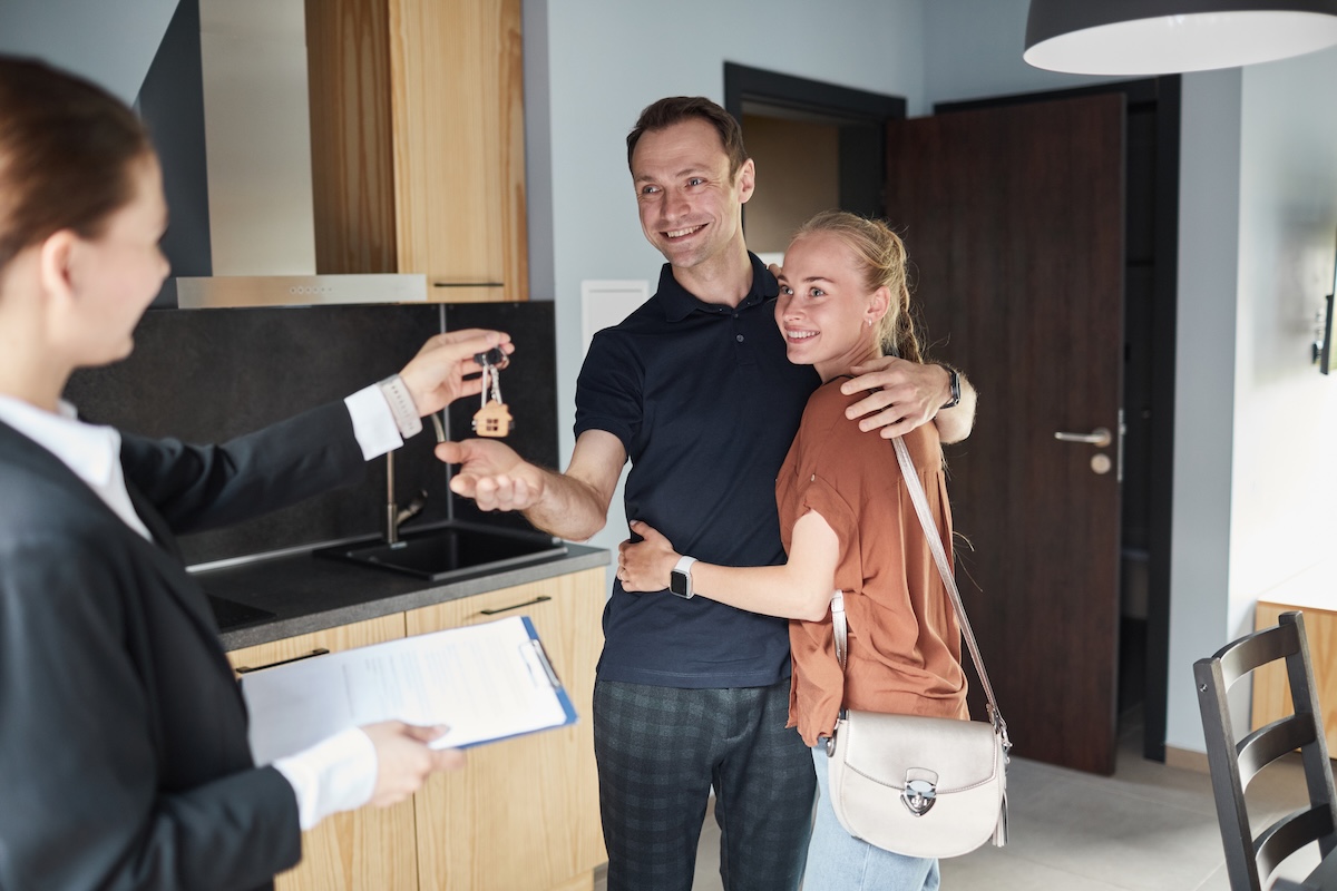 Real estate agent adept at selling new construction homes handing a couple the keys to their new home