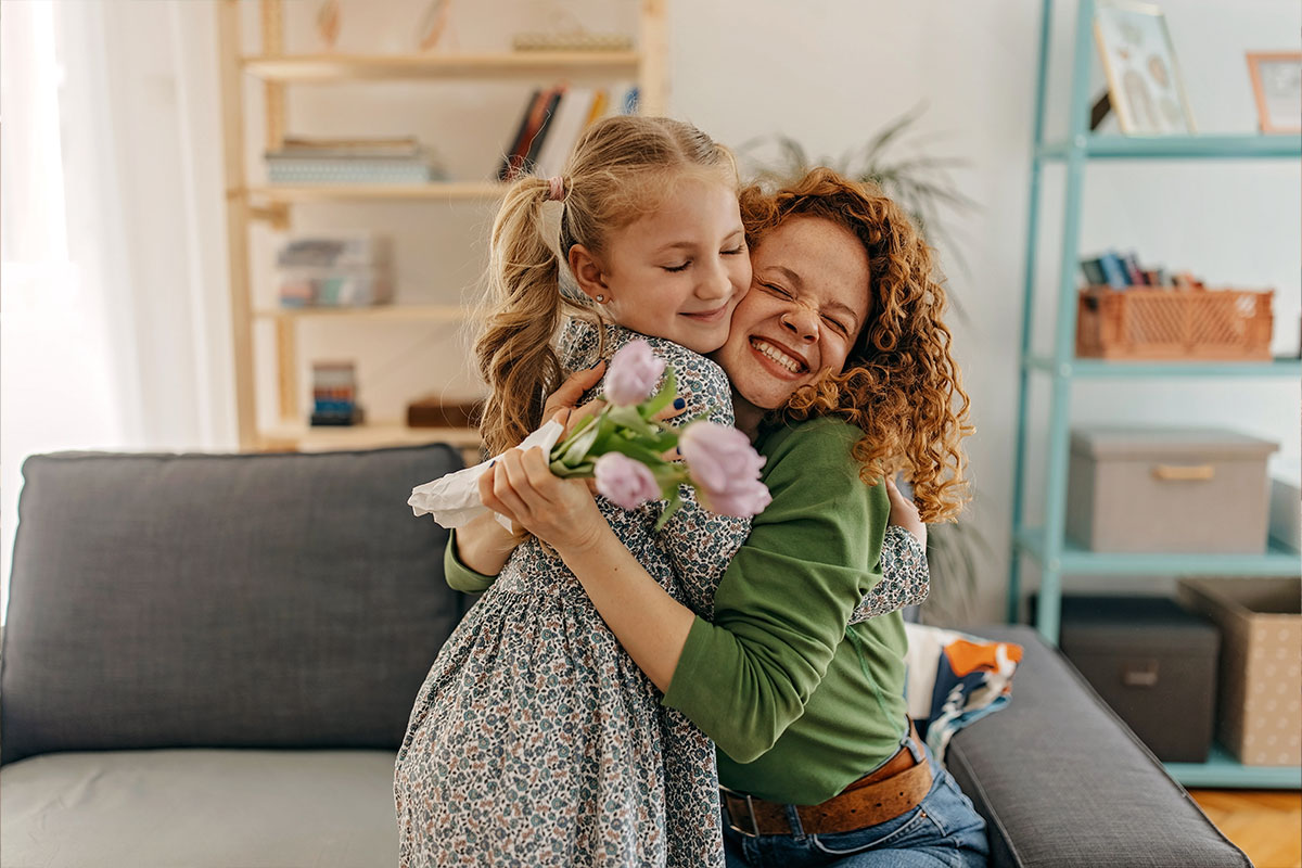 A mother holding a bouquet of flowers and hugging her daughter