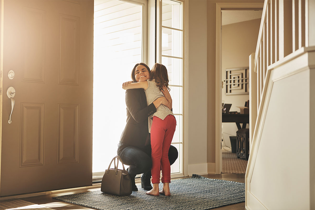 A mom hugging her daughter in the front entry of a home
