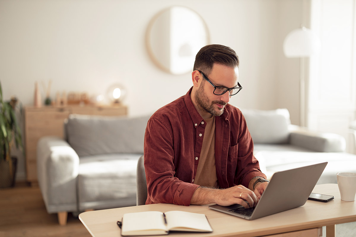 A man working from home, in his living room, using a laptop.