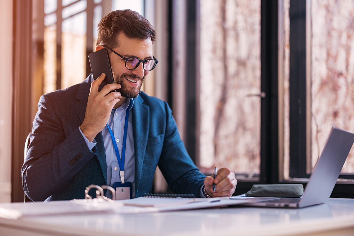 A real estate agent speaking on the phone and sitting in front of his laptop