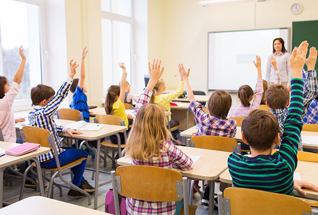 Kids raising their hands while sitting at desks in school