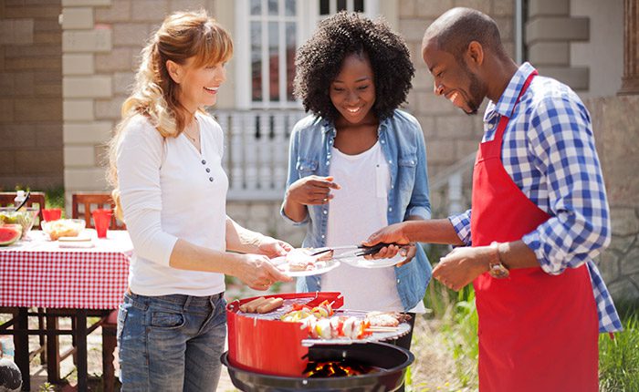 Three people gathered around grill in backyard