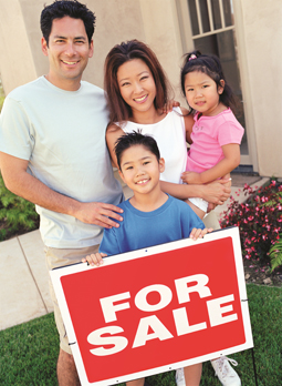 Family of four standing behind For Sale sign