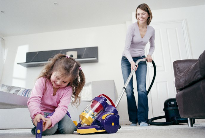 Mother vacuuming while daughter plays with toy vacuum