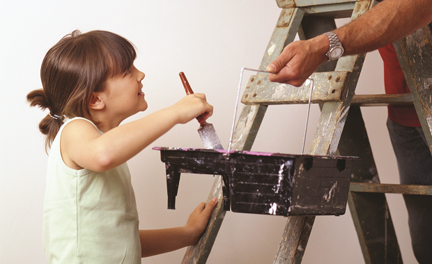 A child with paintbrush standing next to a ladder