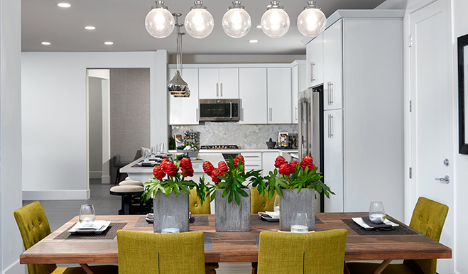 Three vases of flowers in a horizontal line on a wooden kitchen table