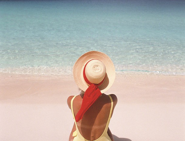 Back view of a woman in a sunhat sitting in front of the ocean