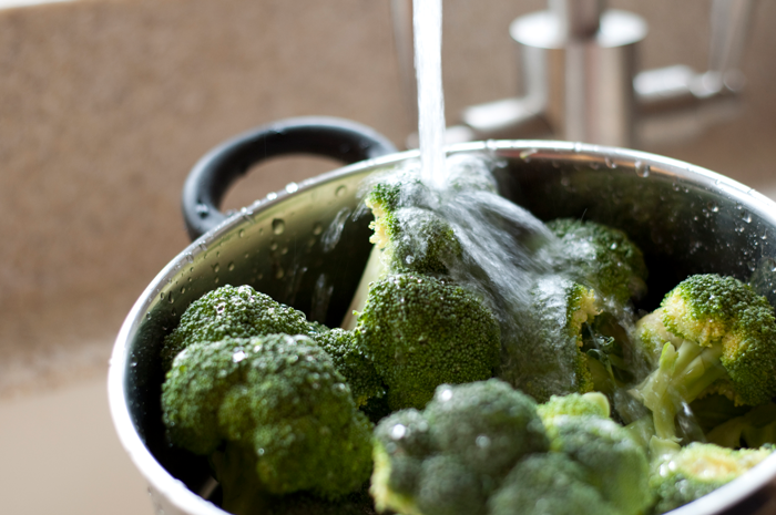 Broccoli being washed in colander in sink