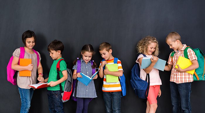 Six children with backpacks in front of a chalkboard