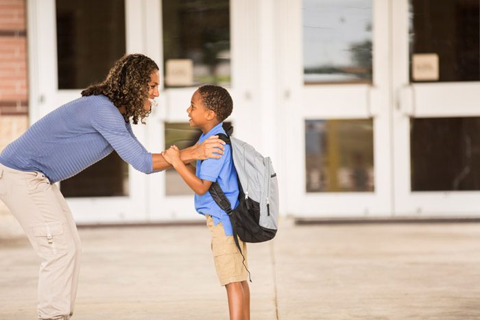 Mother and child with backpack standing in front of school