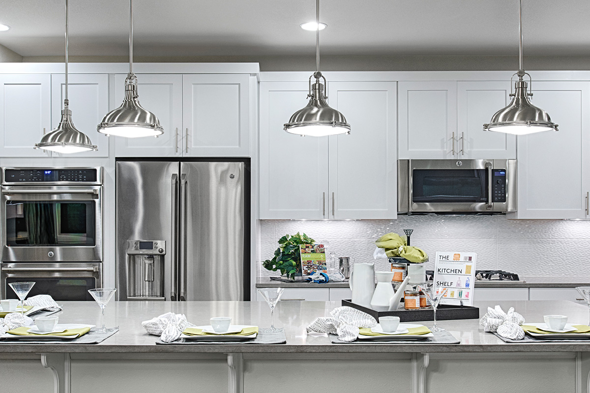 Fresnel pendant lights over island in kitchen with white cabinets and stainless-steel appliances