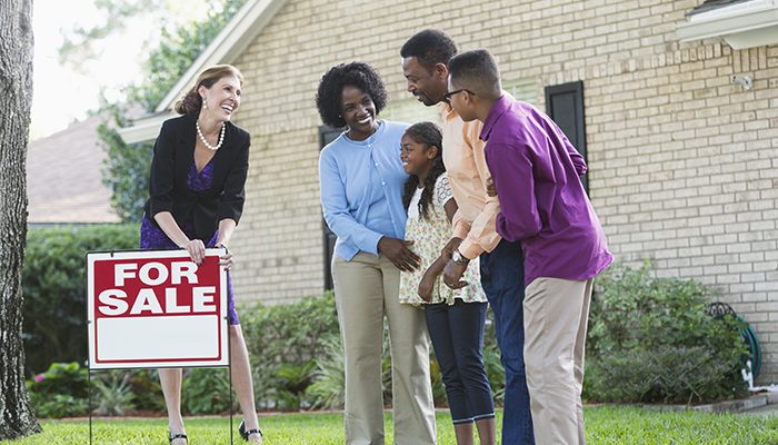 Family and real estate agent standing near For Sale sign
