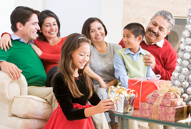 Girl unwrapping presents while surrounded by extended family