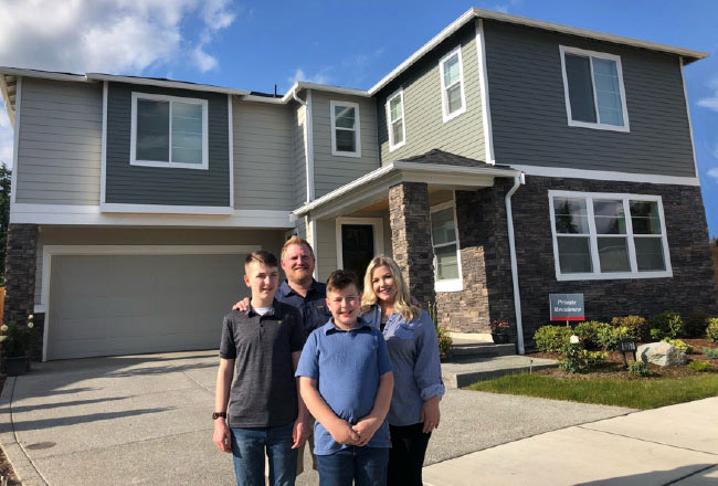 Family of four posing in front of their new two-story home