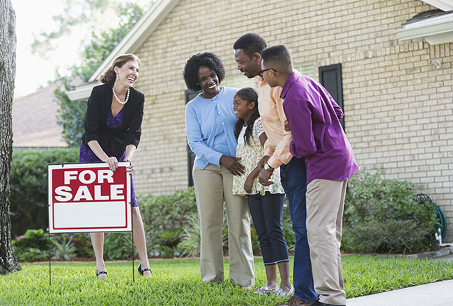 Family and real estate agent standing near For Sale sign