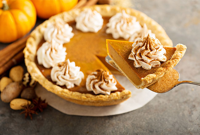 Pumpkin pie with a slice on a serving knife