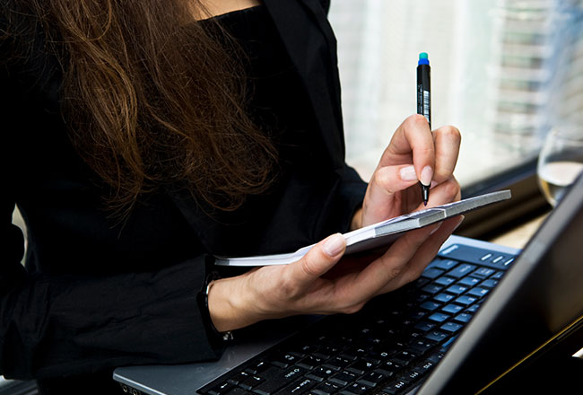 Woman jotting something on notepad while looking at computer