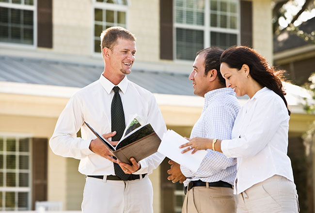 Couple standing with real estate agent in front of a home