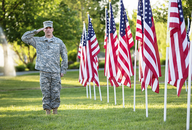 Saluting soldier standing next to a line of American flags
