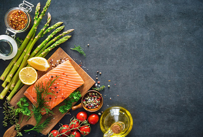 Asparagus, fish, tomatoes, oil and other ingredients on a black background