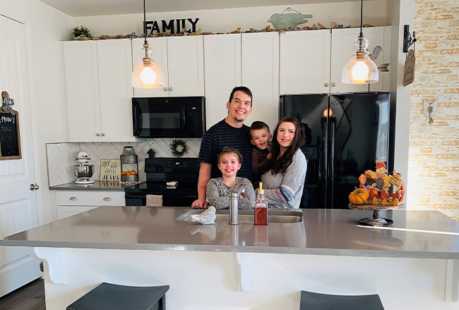 Family of four standing in kitchen with white cabinets and black appliances