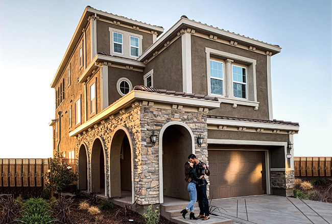 Couple kissing in front of covered entry of three-story home with stone accents