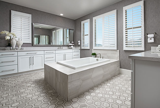 Freestanding tub in center of owner's bathroom with white cabinets and hexagonal floor tile