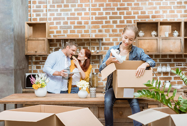 Teen holding moving box and parents in the background