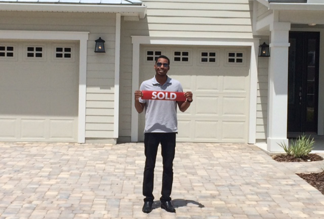 Homebuyer standing on driveway holding sold sign
