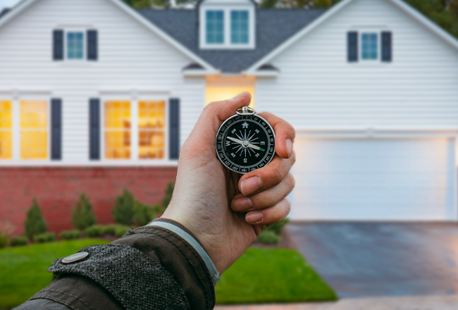 Hand holding compass in from of a home