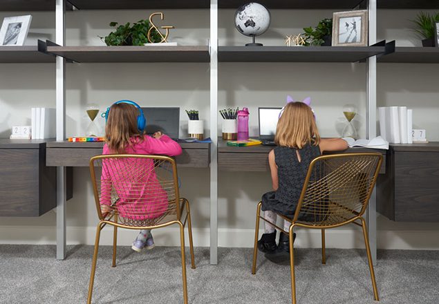 Two young girls sitting at side-by-side desks doing virtual learning