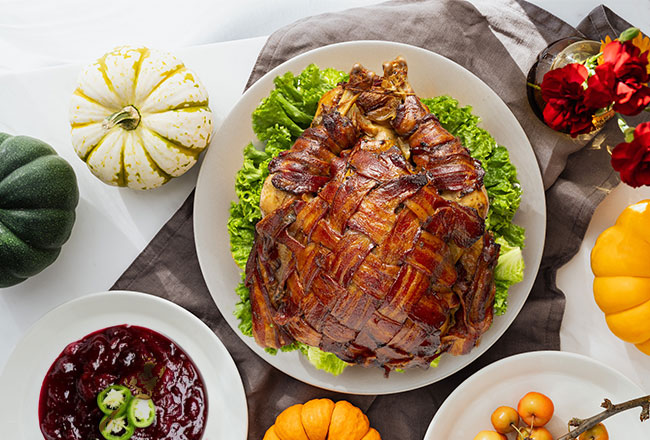 Turkey sitting on a bed of lettuce, surround by dourds and Thanksgiving sides