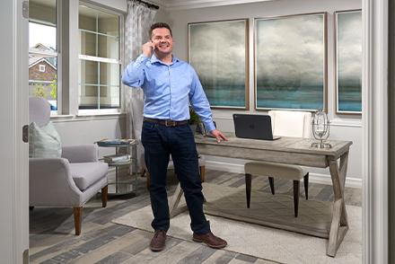 Man standing in home office smiling and talking on cell phone.