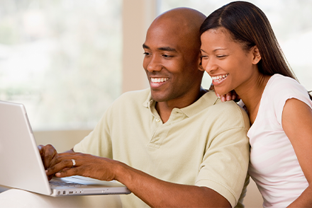 Man typing on laptop with women smiling, looking over his shoulder