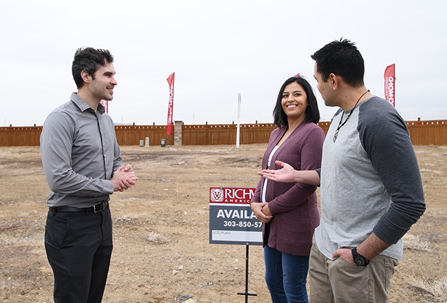 Happy homebuyers standing with their sales associate in front of the homesite they've selected