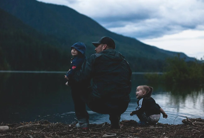 Father kneeling at edge of river with with son and daughter